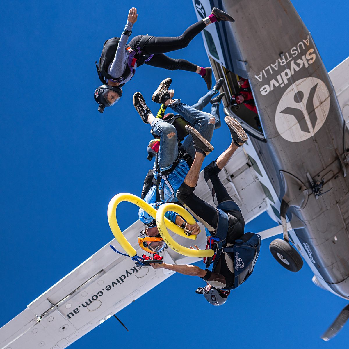 Skydivers leaving the wing strut of the aircraft trailing yellow rings
