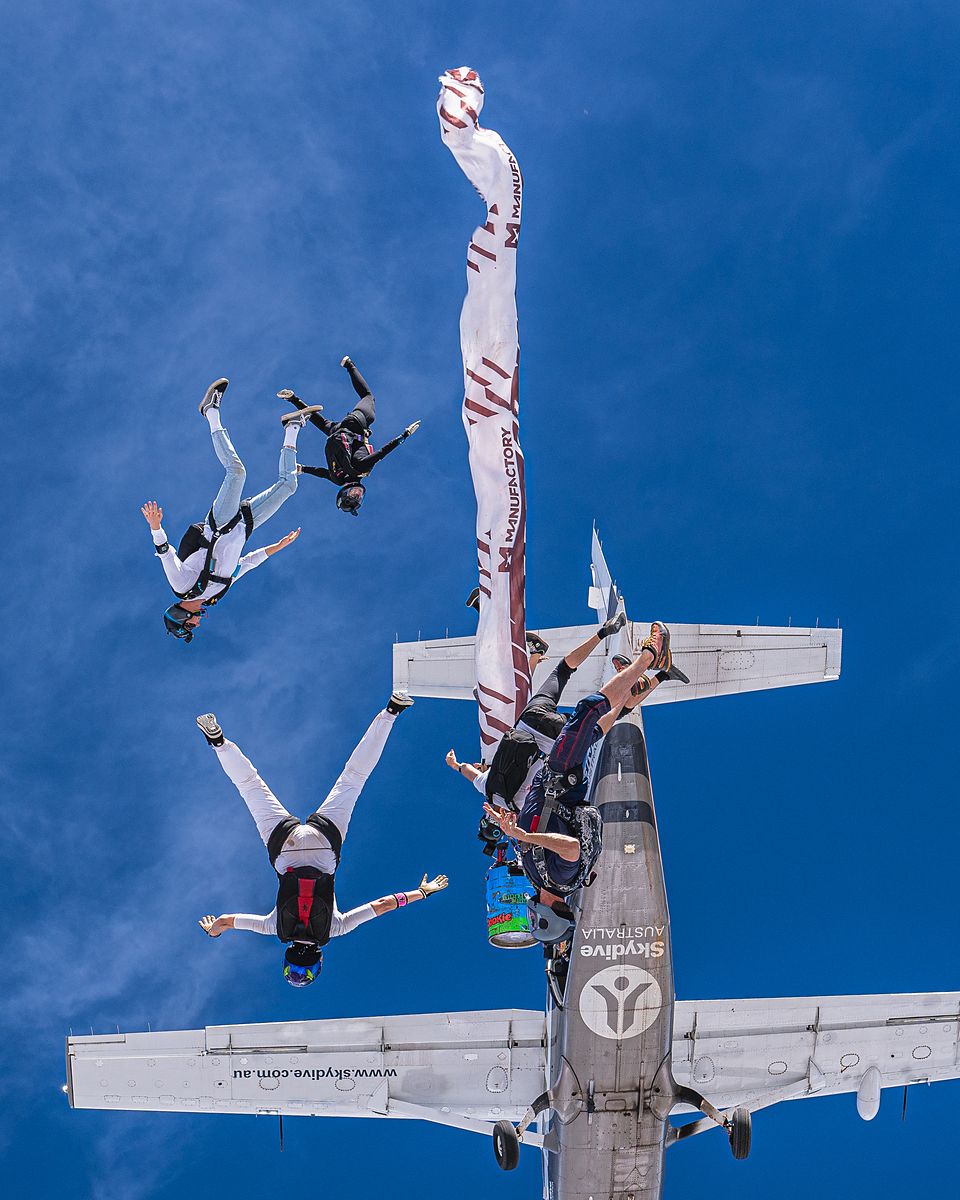 Skydivers exiting past the tail with a banner streaming behind
