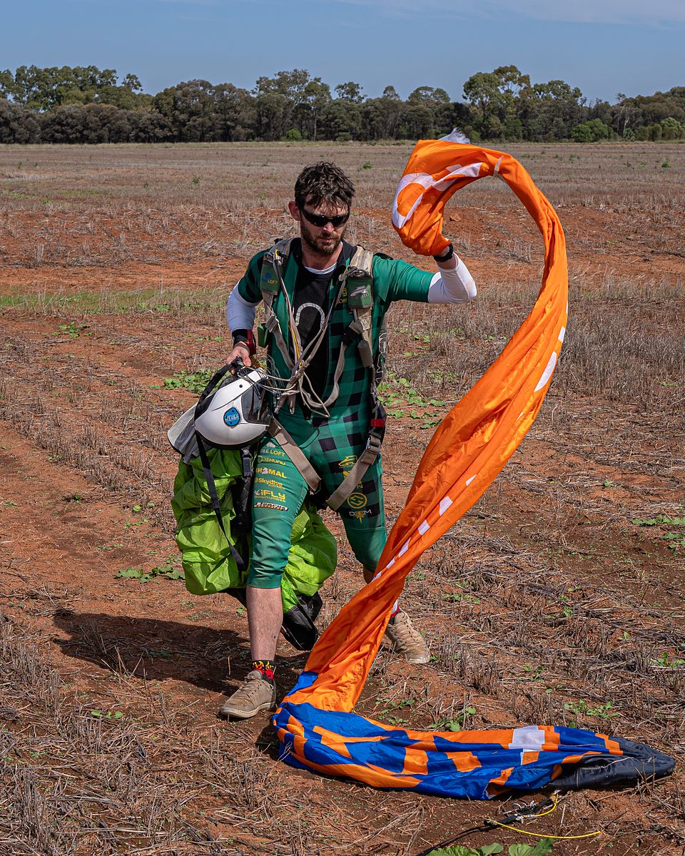 A jumper walking in from the landing area trailing an orange canopy