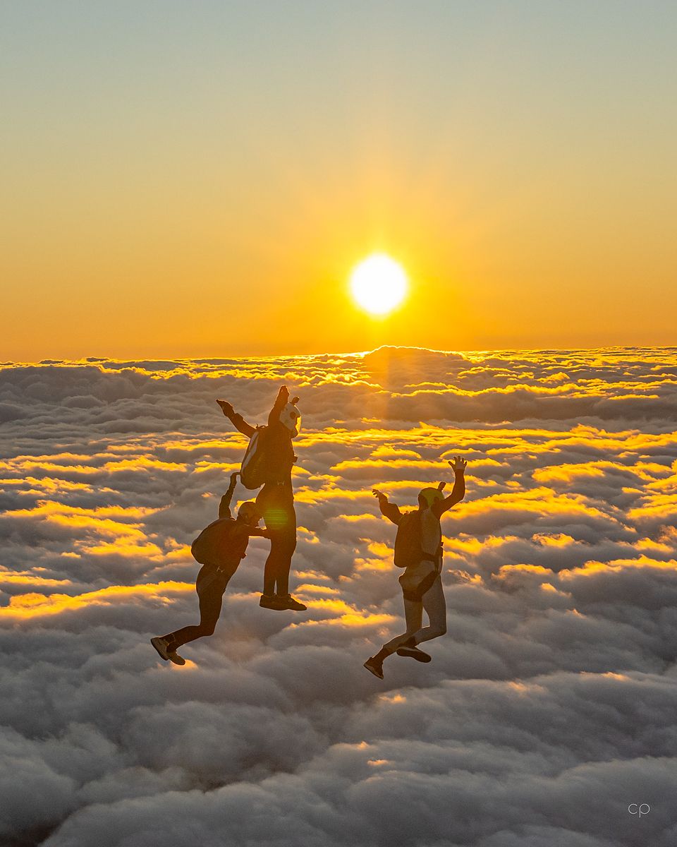 Two skydivers silhouetted against the sun above a deck of cloud