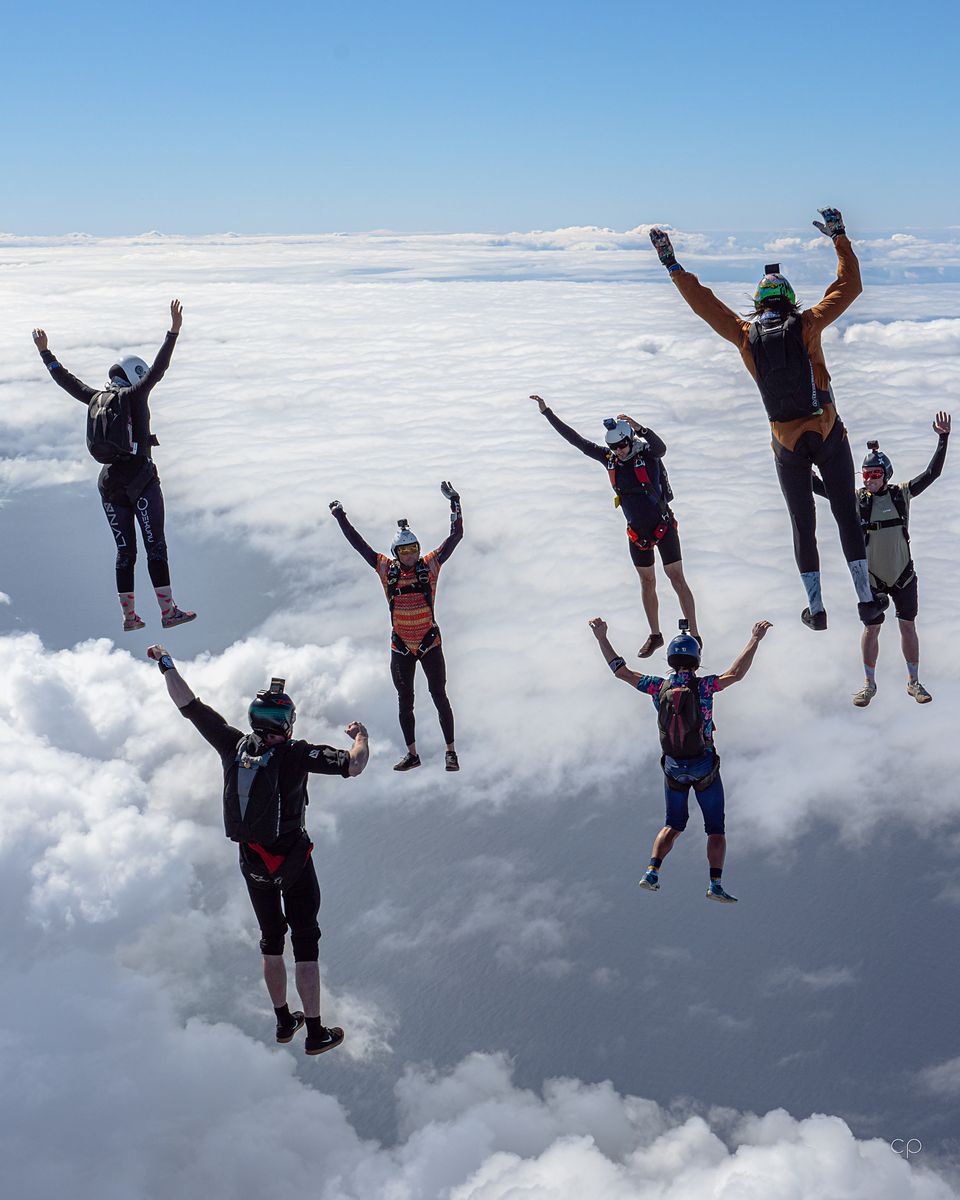 A group flying belly-down with arms raised above a solid cloud layer