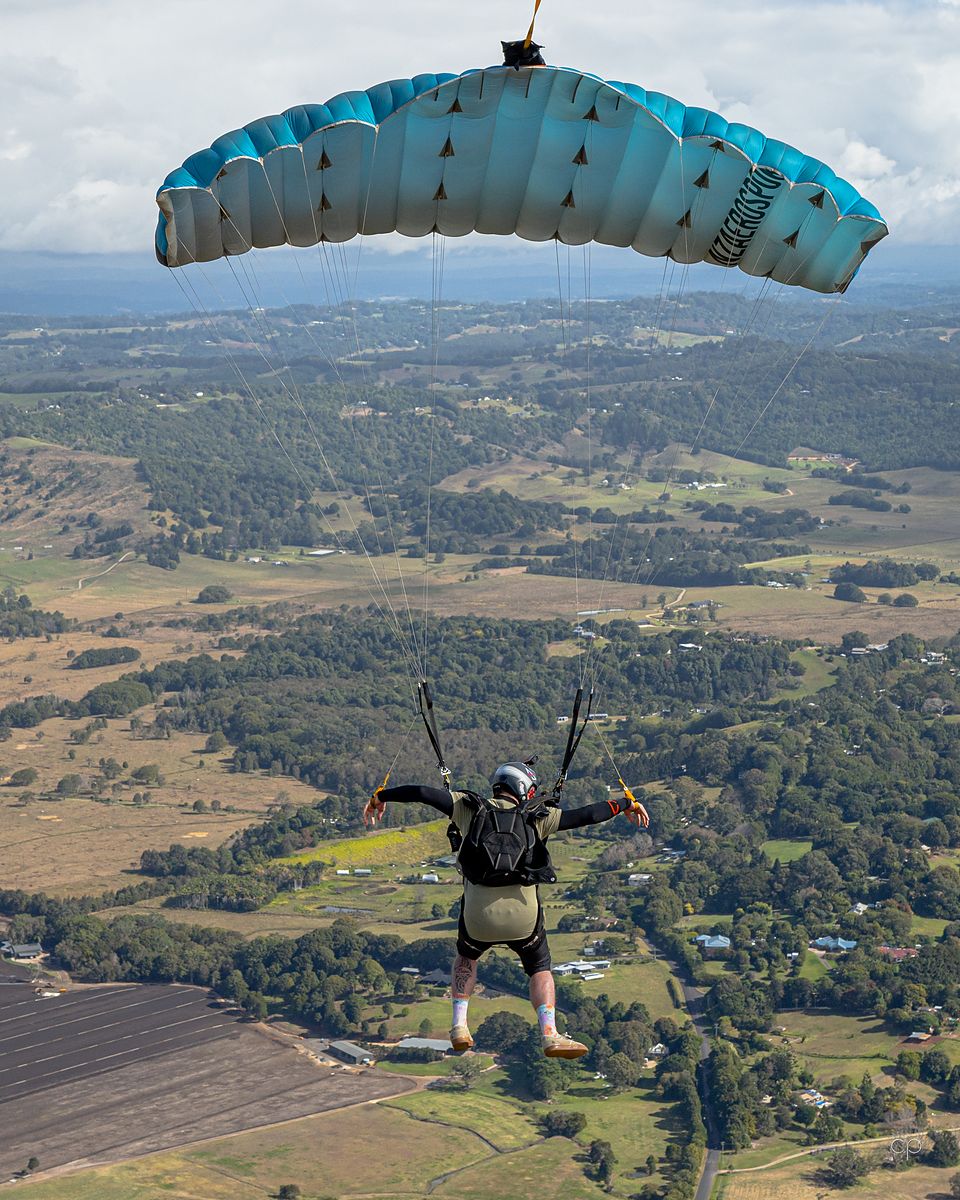 A skydiver under a teal canopy above green farmland