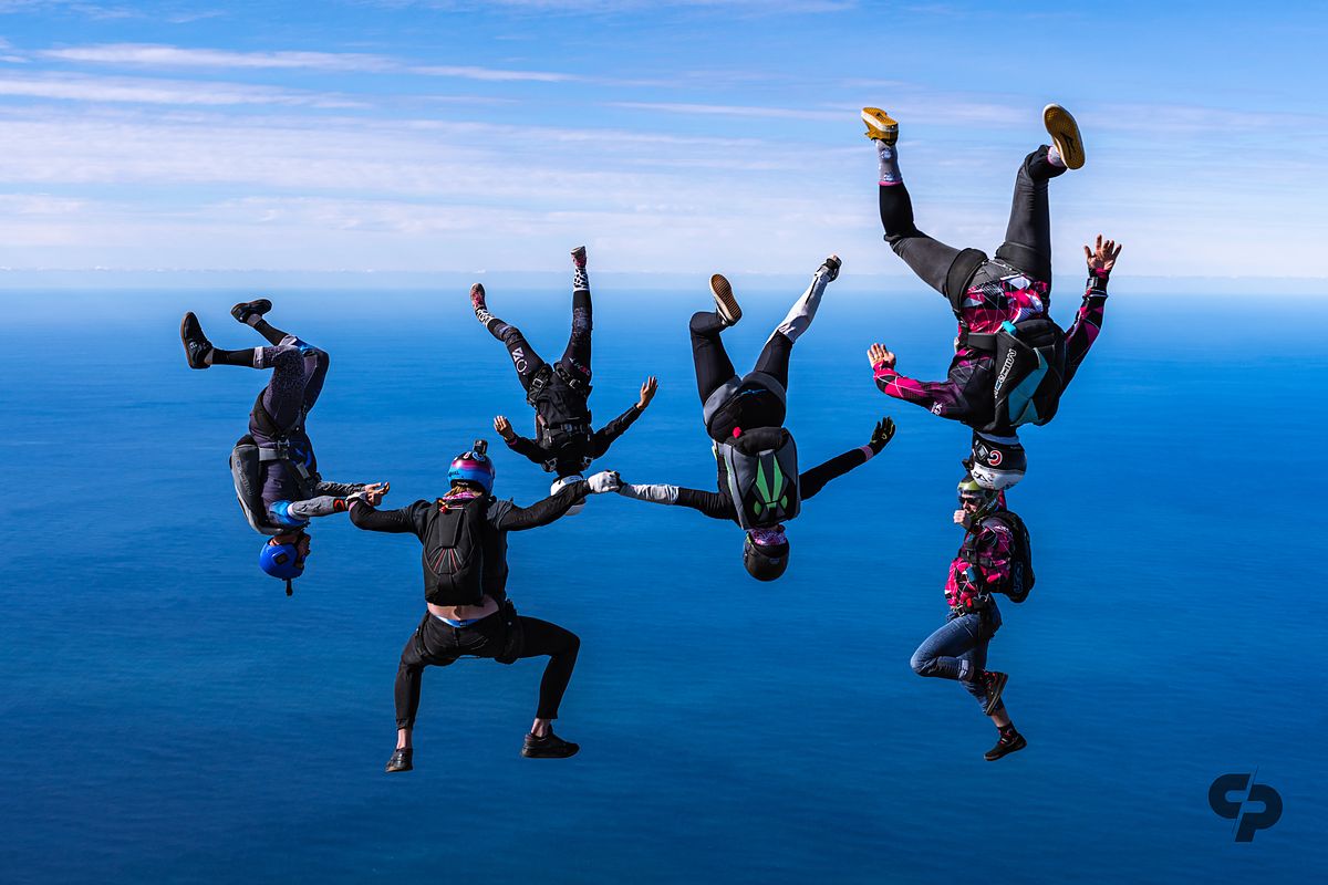 A line of head-down flyers against blue sky over the ocean