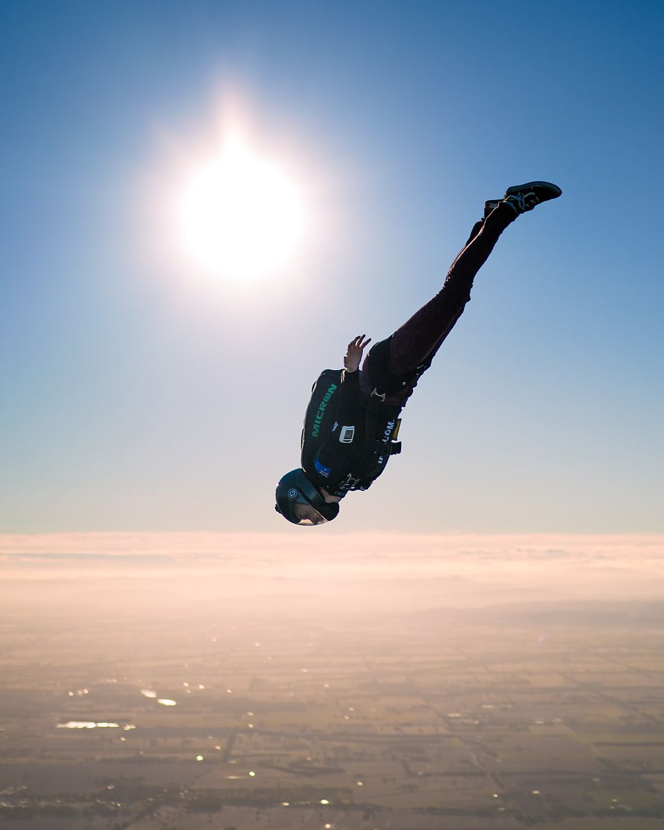 A lone skydiver in freefall silhouetted against the sun