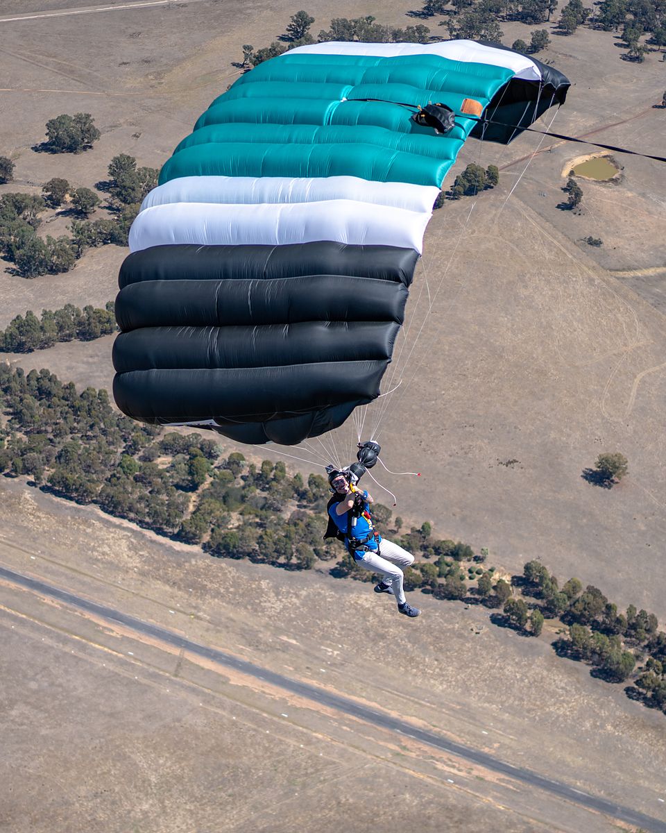 A skydiver under a teal canopy above farmland